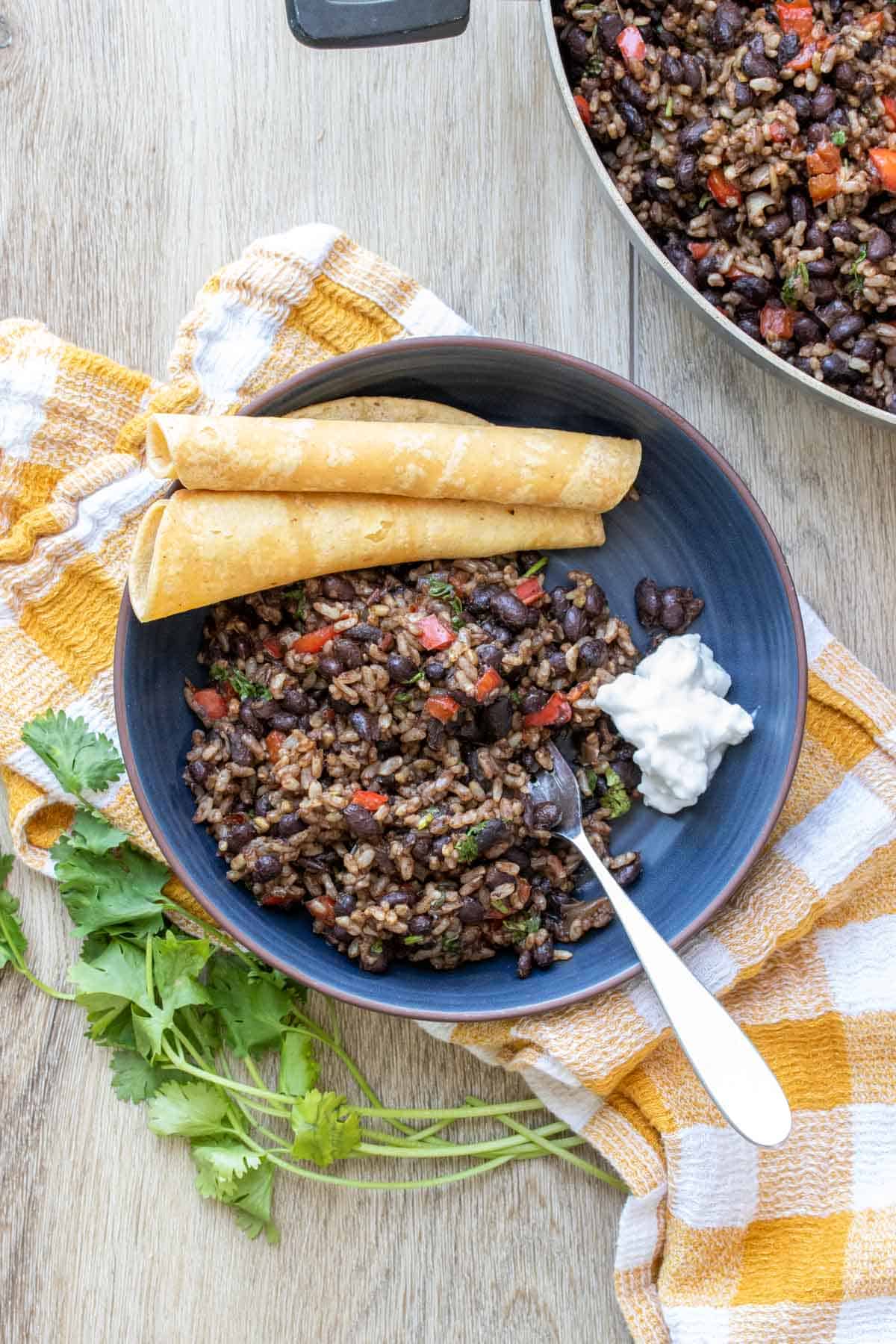 Dark blue bowl with a black bean and rice mix inside next to corn tortillas and sour cream