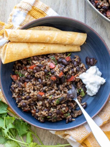 Blue bowl with a black bean and rice mixture in it on a yellow and white checkered towel.