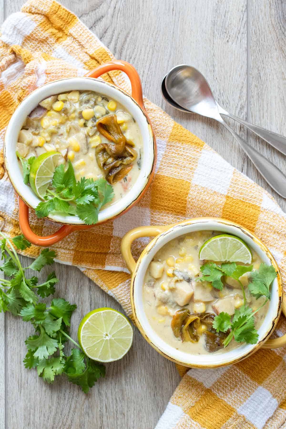 Two bowls on a yellow and white checkered towel filled with a creamy corn and pepper soup