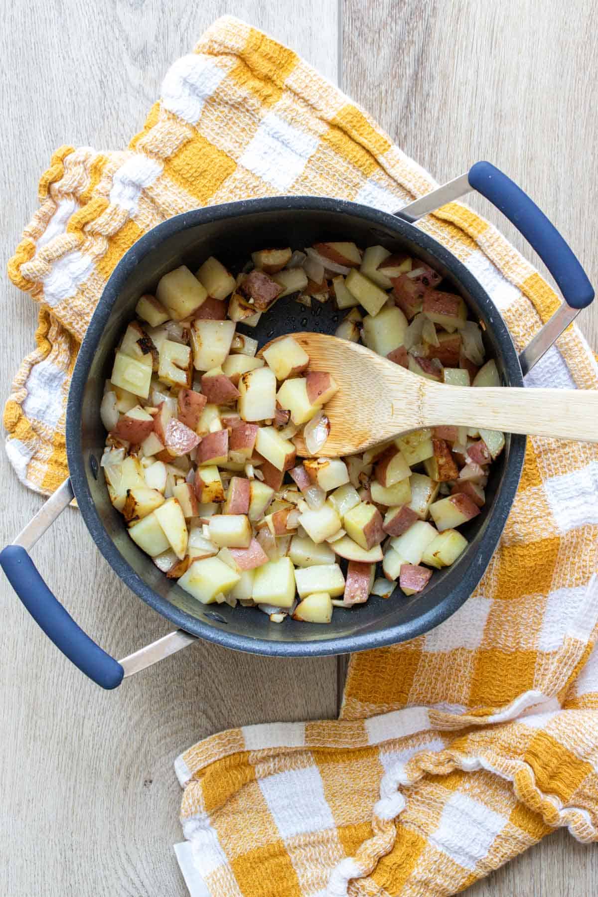 Wooden spoon mixing chopped potatoes in a pot.