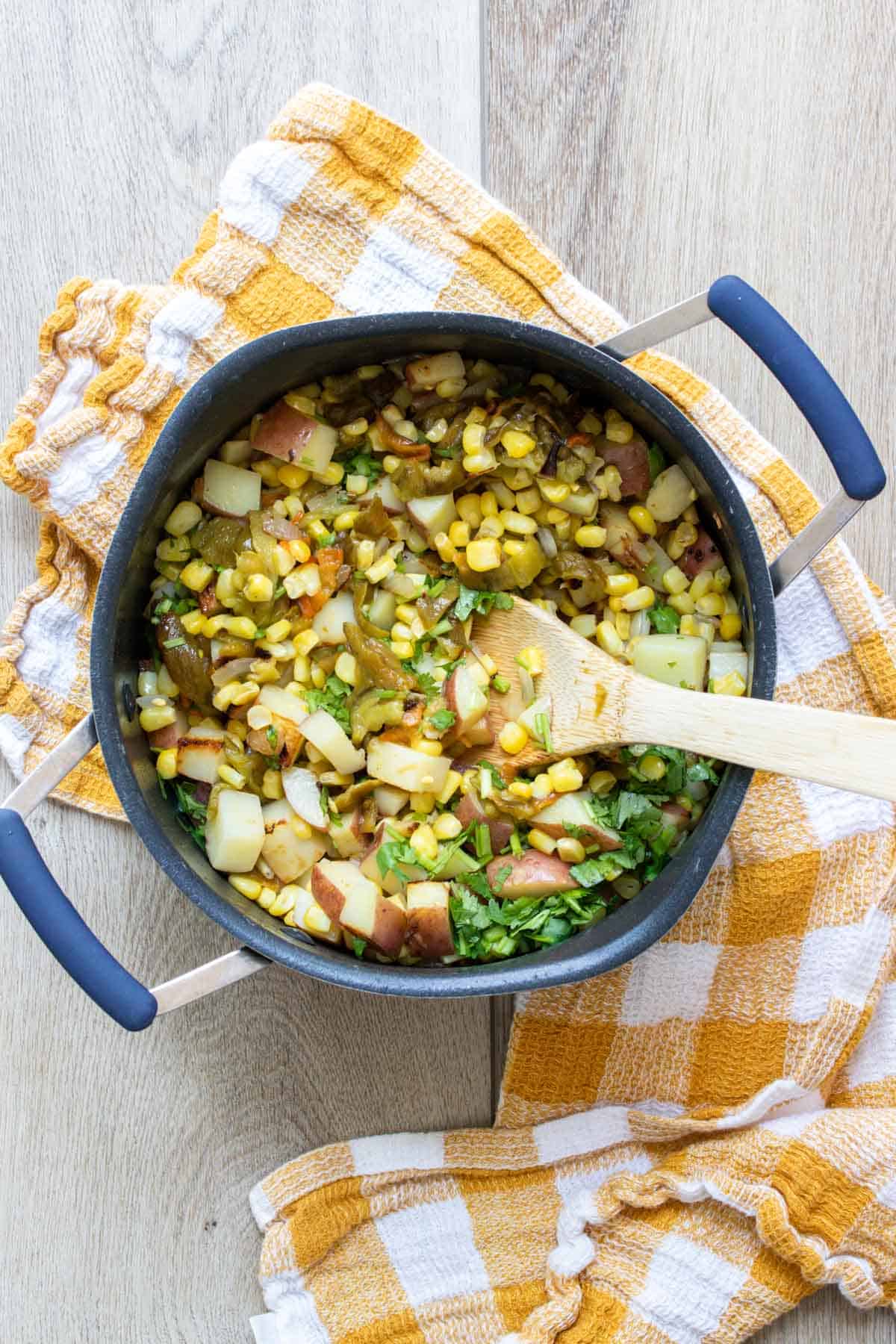 Wooden spoon mixing chopped potatoes, corn and peppers in a pot