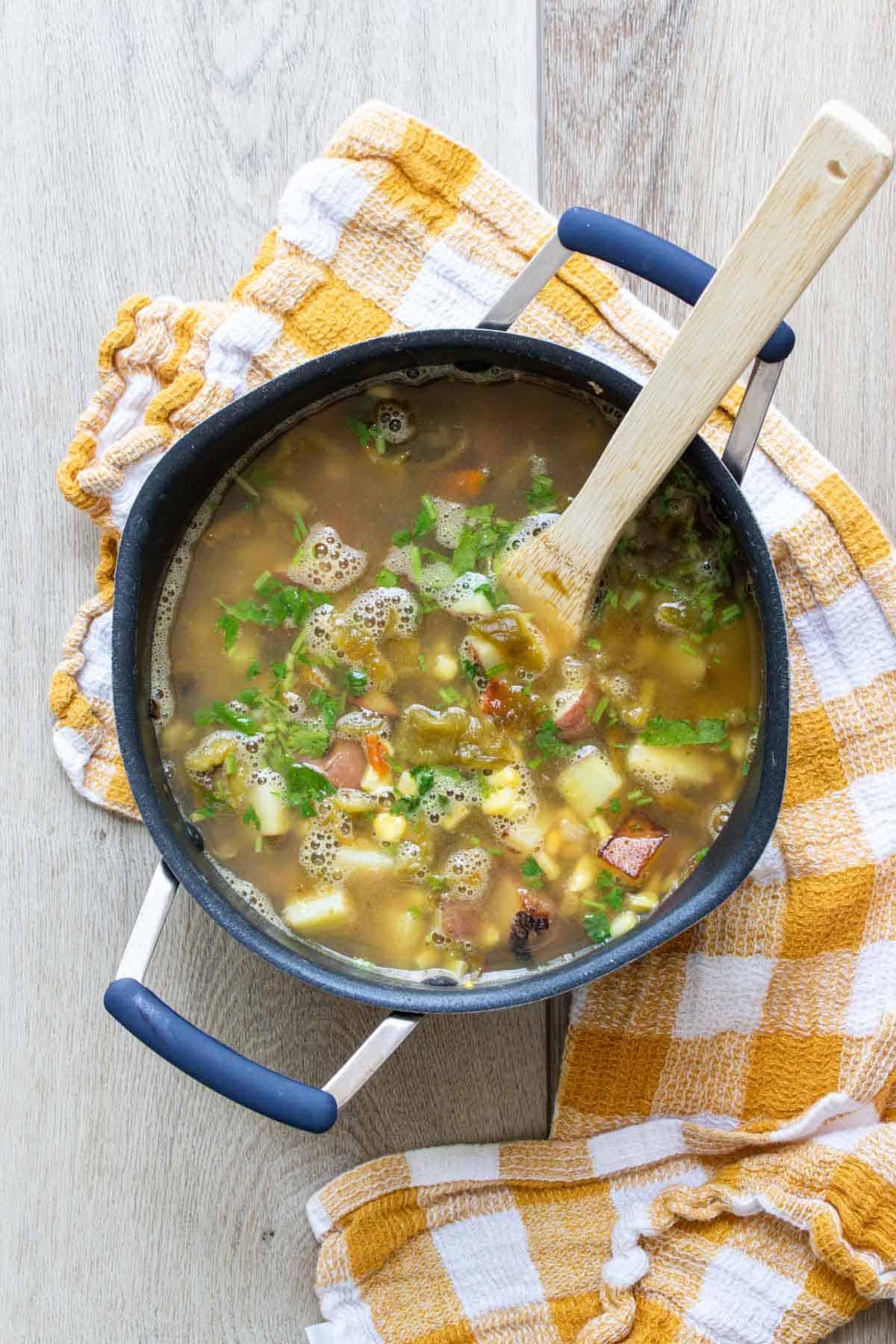 Wooden spoon stirring a veggie broth soup with herbs in a pot.