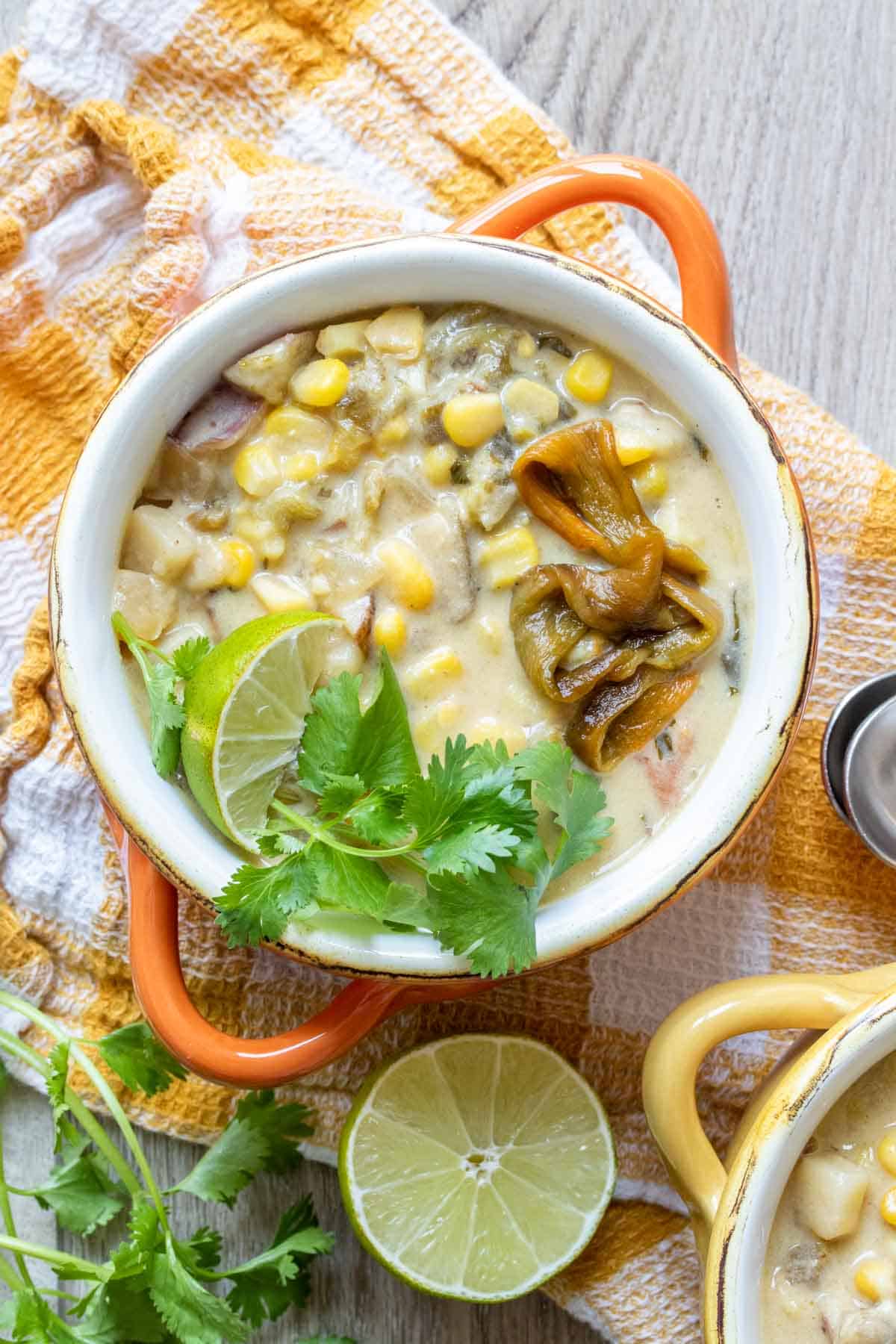 Orange soup bowl with a creamy corn and pepper soup on a checkered towel.