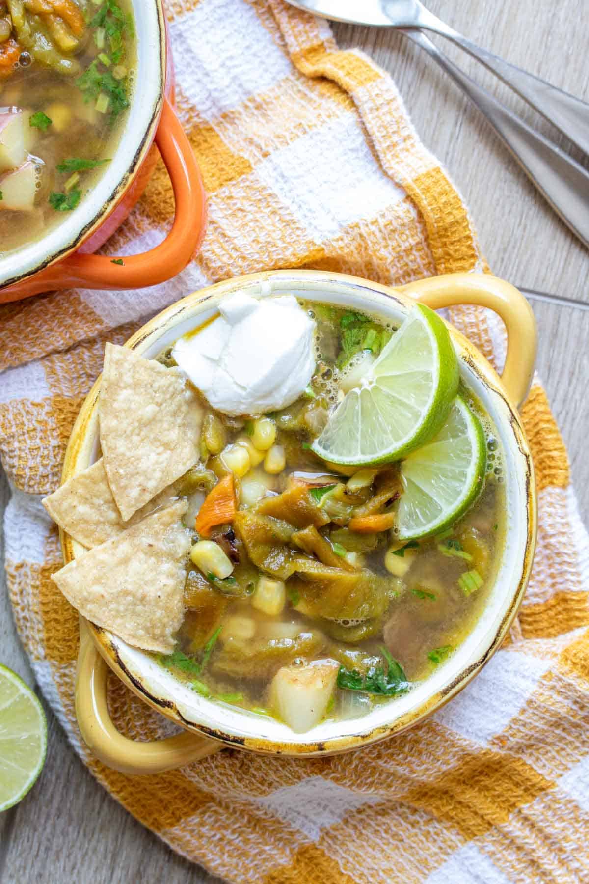 A broth based soup with corn, potatoes and peppers topped with lime, sour cream and chips.