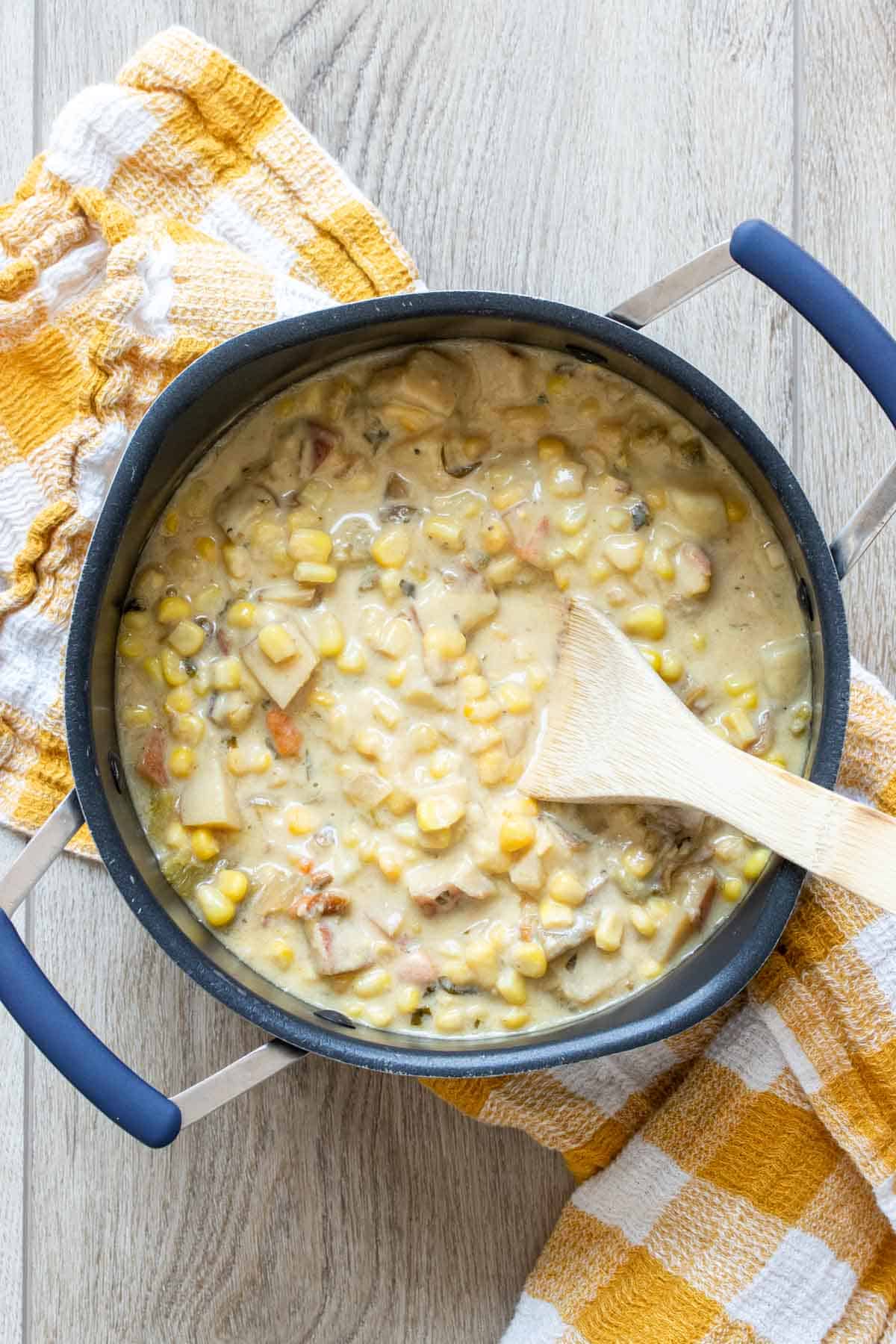 Wooden spoon mixing a creamy corn, potato and pepper soup in a pot.