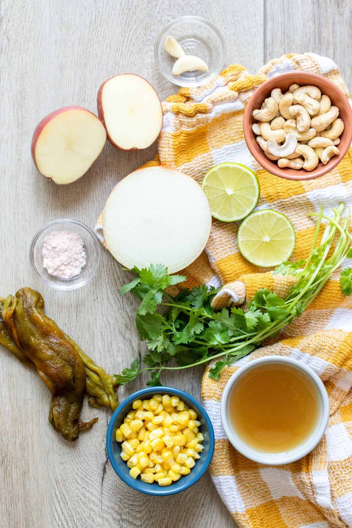 Ingredients needed for a vegan corn, potato and poblano chowder on a light wooden surface with a checkered towel