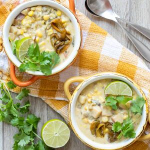 Orange and yellow bowls filled with a creamy corn and pepper soup topped with lime wedges and cilantro.