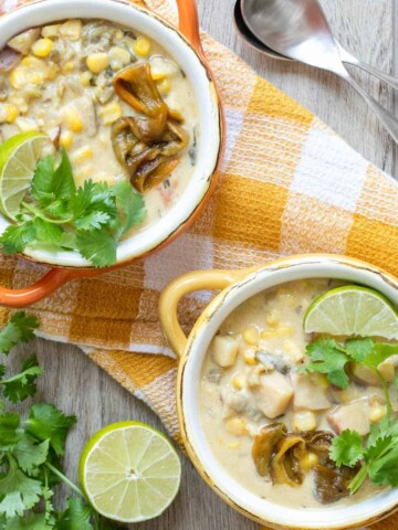 Orange and yellow bowls filled with a creamy corn and pepper soup topped with lime wedges and cilantro.