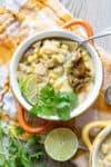 A close up of a poblano corn chowder in an orange soup bowl with a spoon getting a bite.