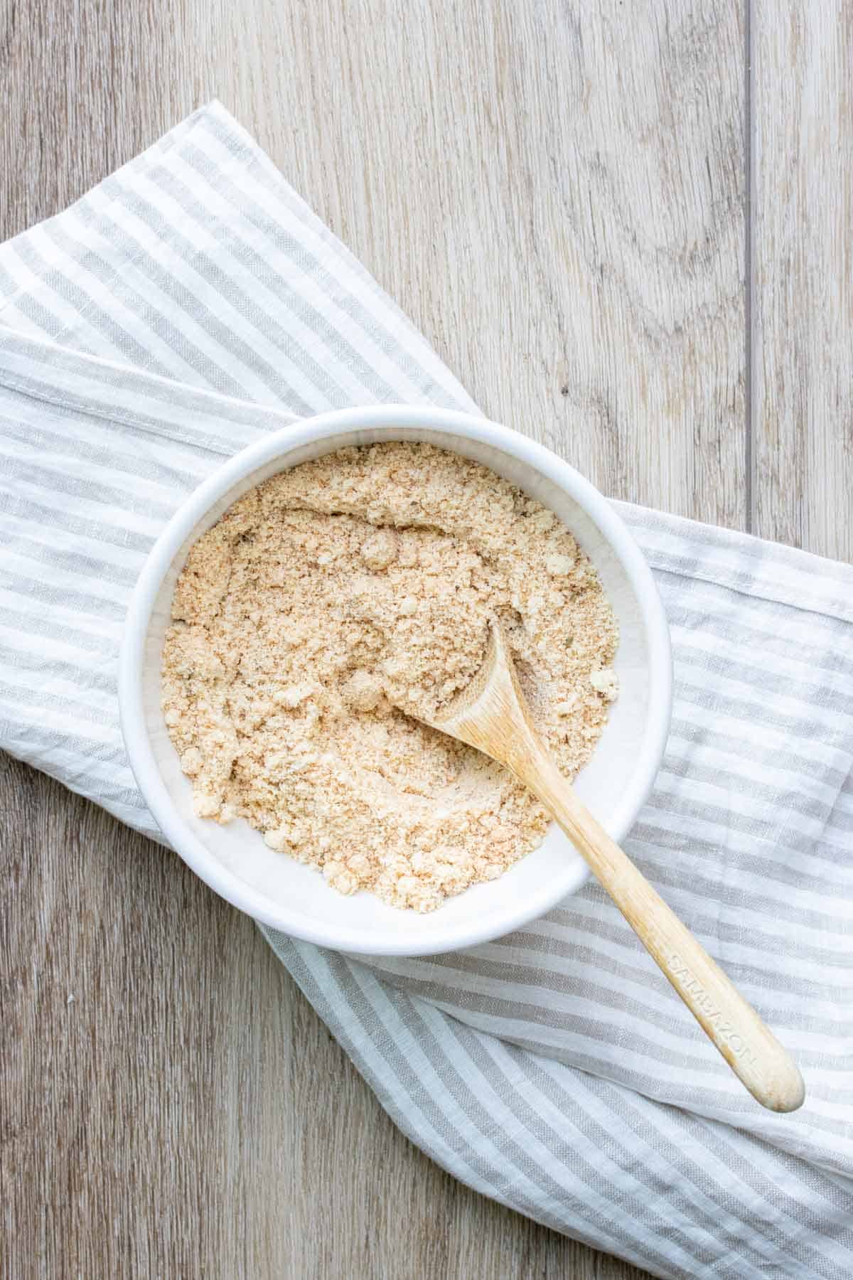 Wooden spoon mixing breadcrumb topping in a white bowl