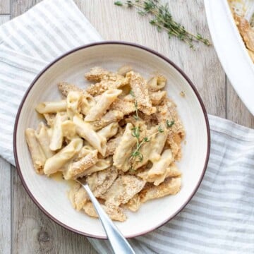 Cream bowl with a creamy pasta dish topped with crispy breadcrumbs on a wooden surface