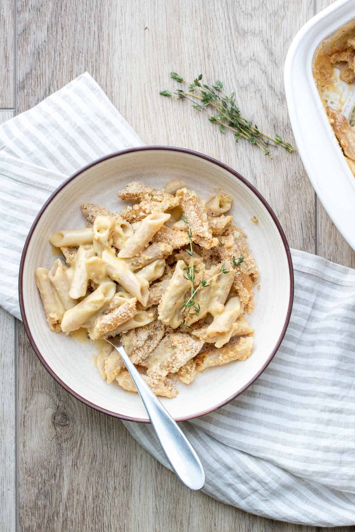 Cream bowl with a creamy pasta dish topped with crispy breadcrumbs on a wooden surface