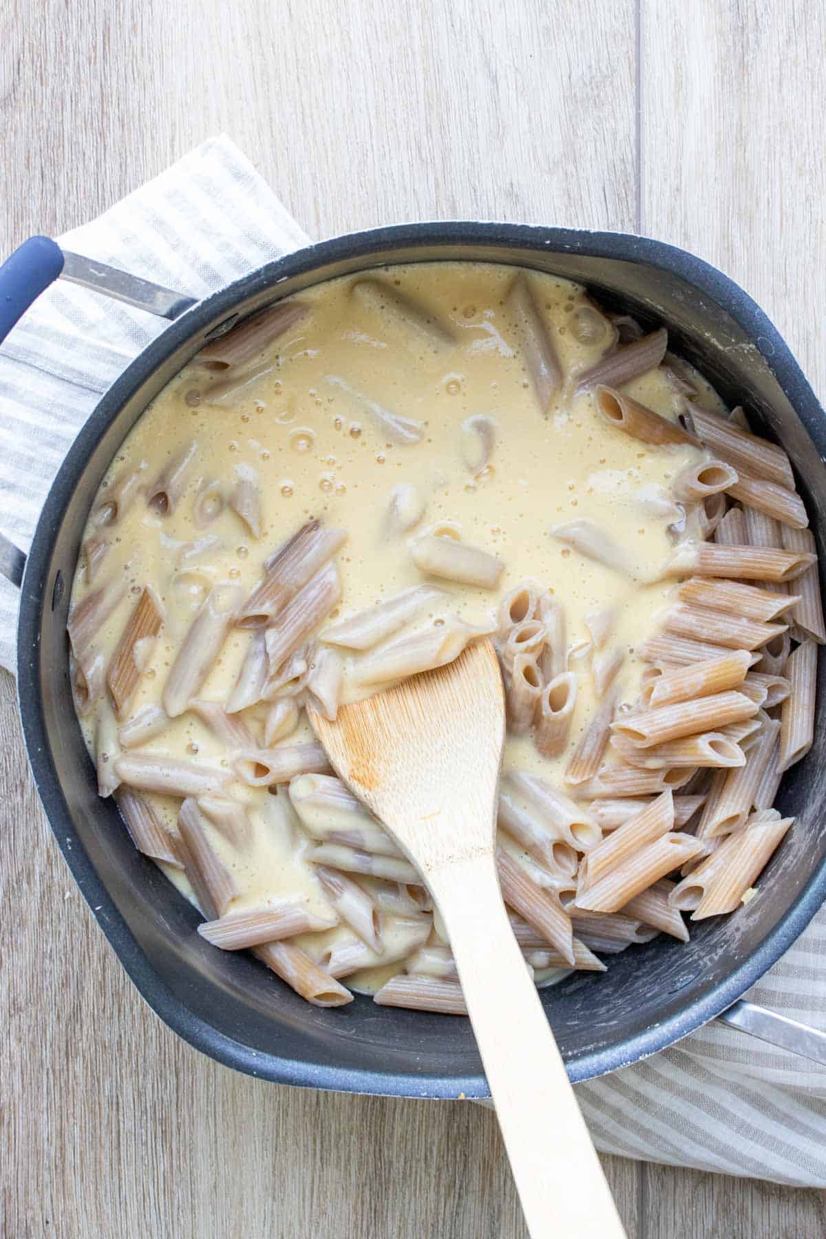 Wooden spoon mixing creamy sauce into a pot of pasta