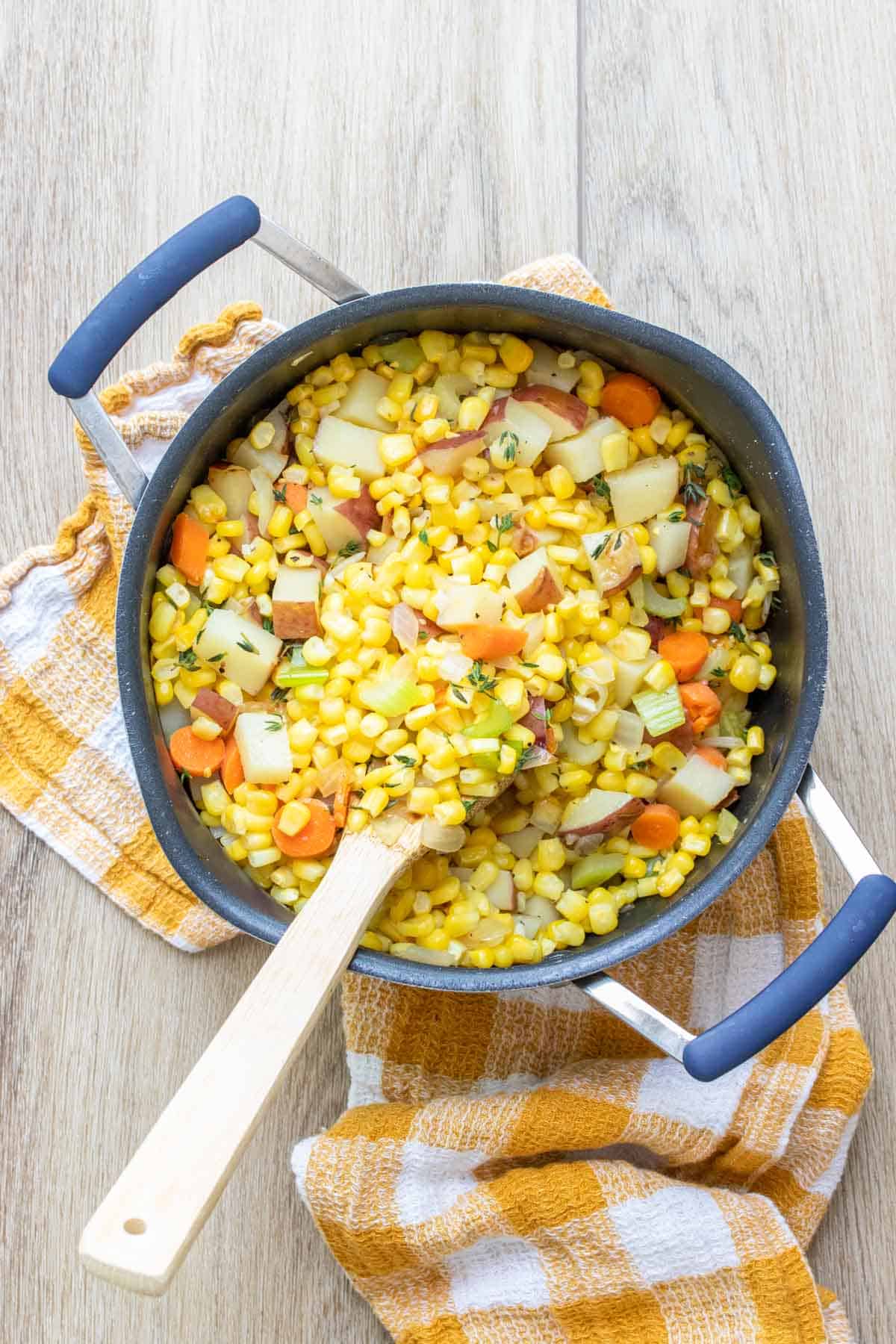 Corn, potatoes and carrots being mixed in a pot by a wooden spoon