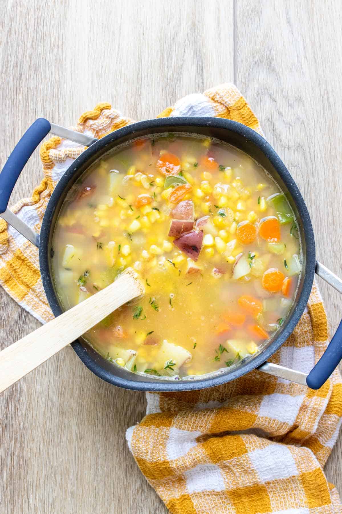 Wooden spoon in a pot filled with a broth , corn, carrots, potatoes and onions