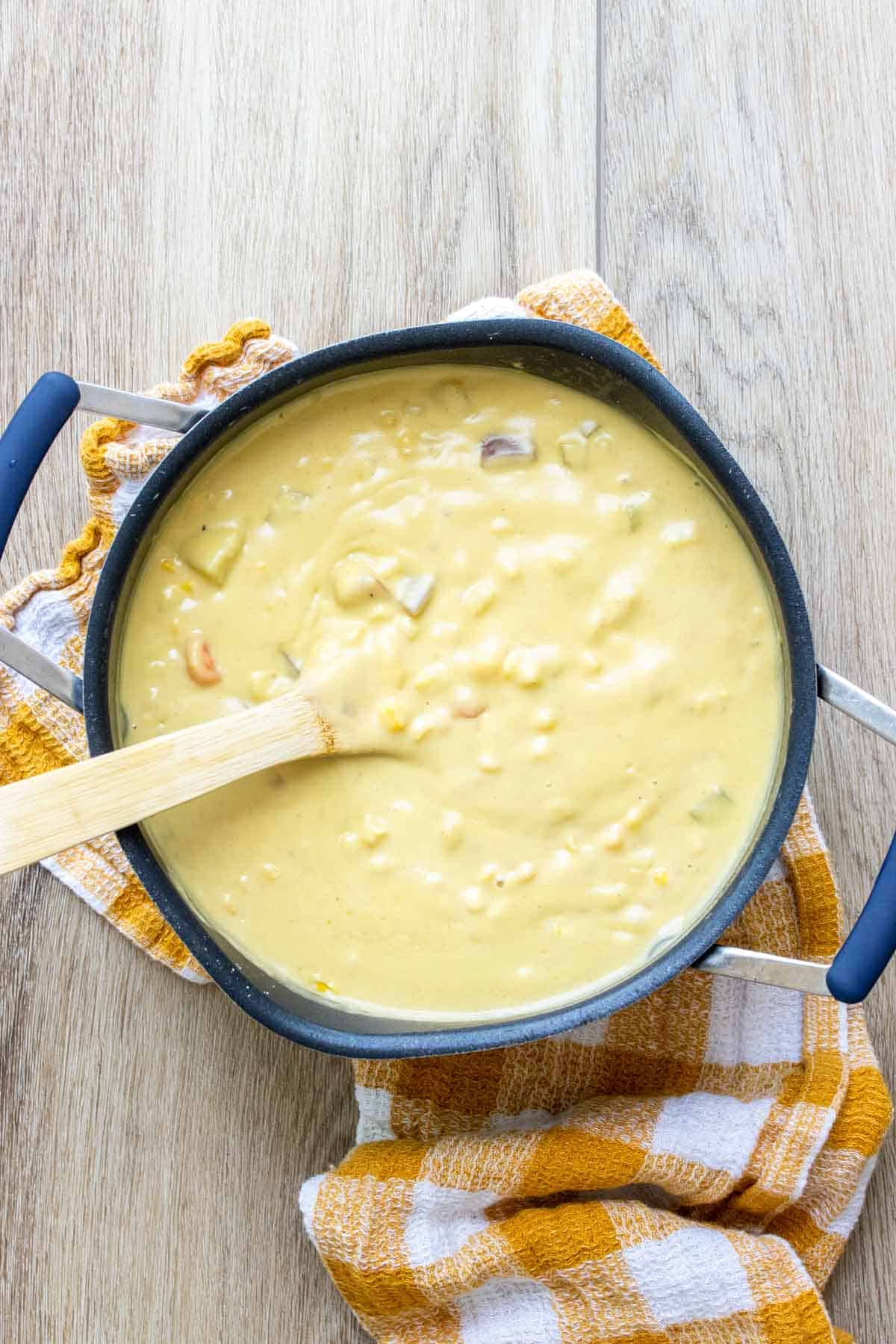 Wooden spoon mixing corn chowder in a black pot