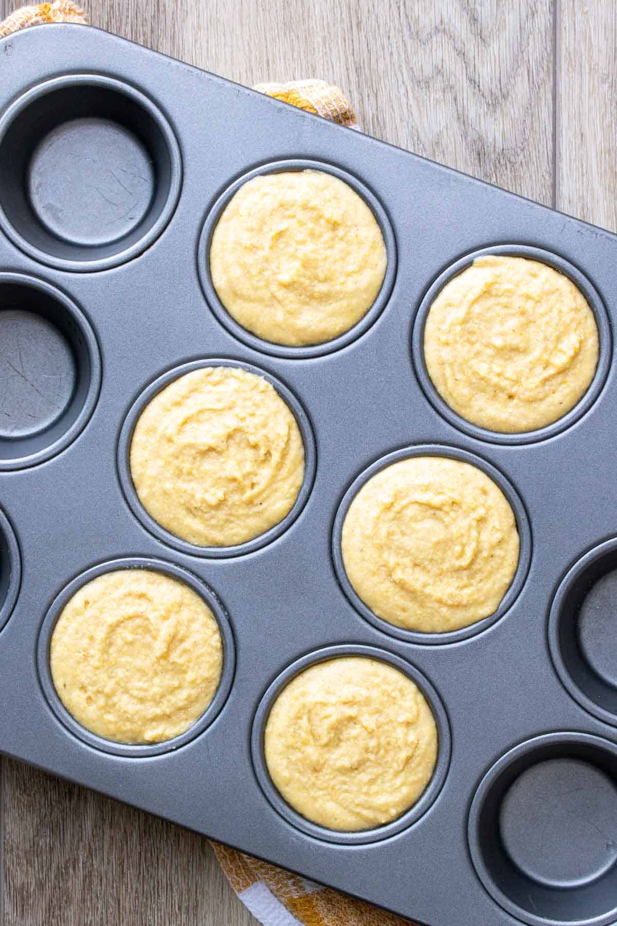 Muffin tin on a wooden surface filled with a yellow batter