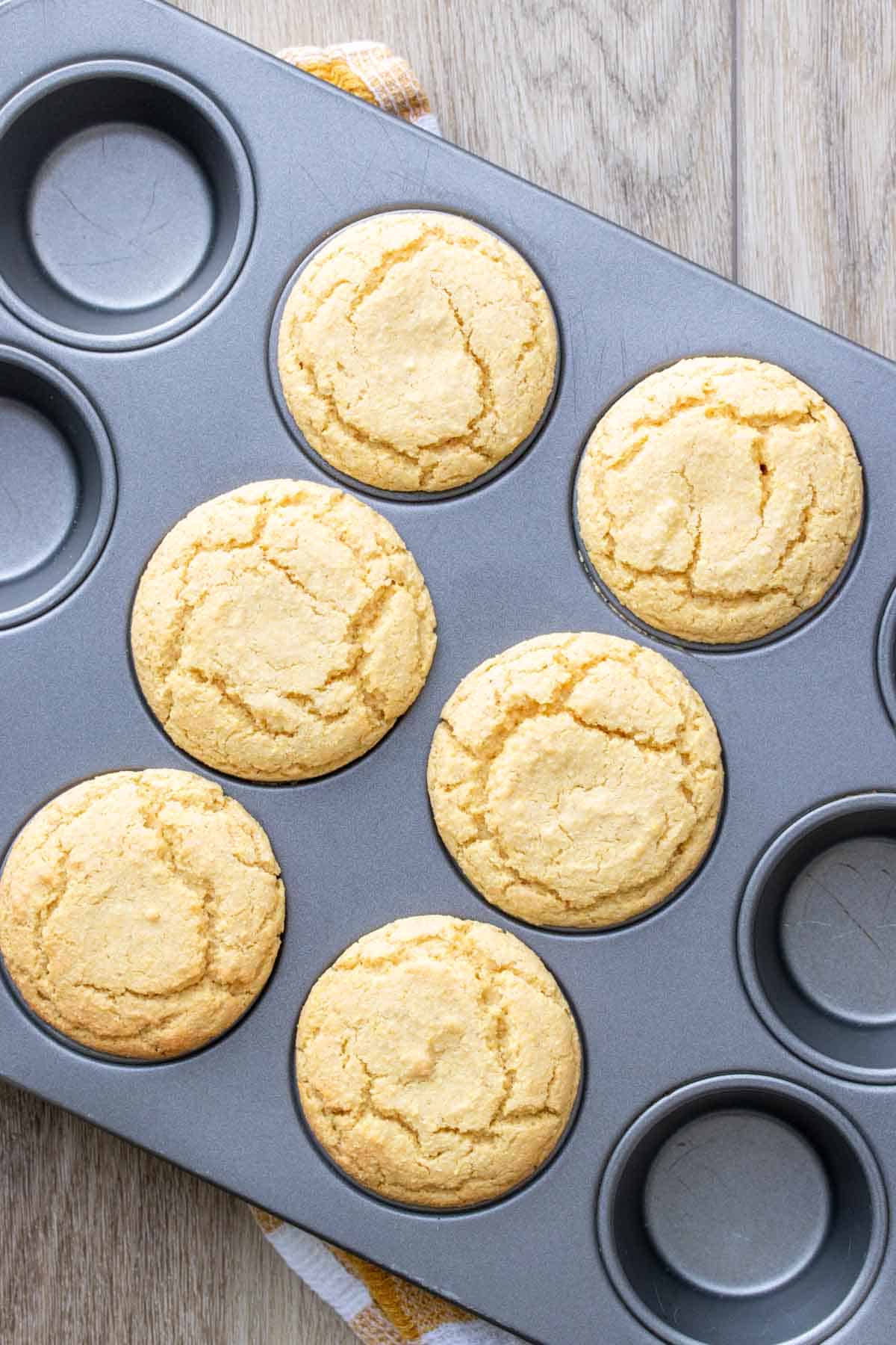 Baked yellow muffins in a muffin tin sitting on a wooden surface