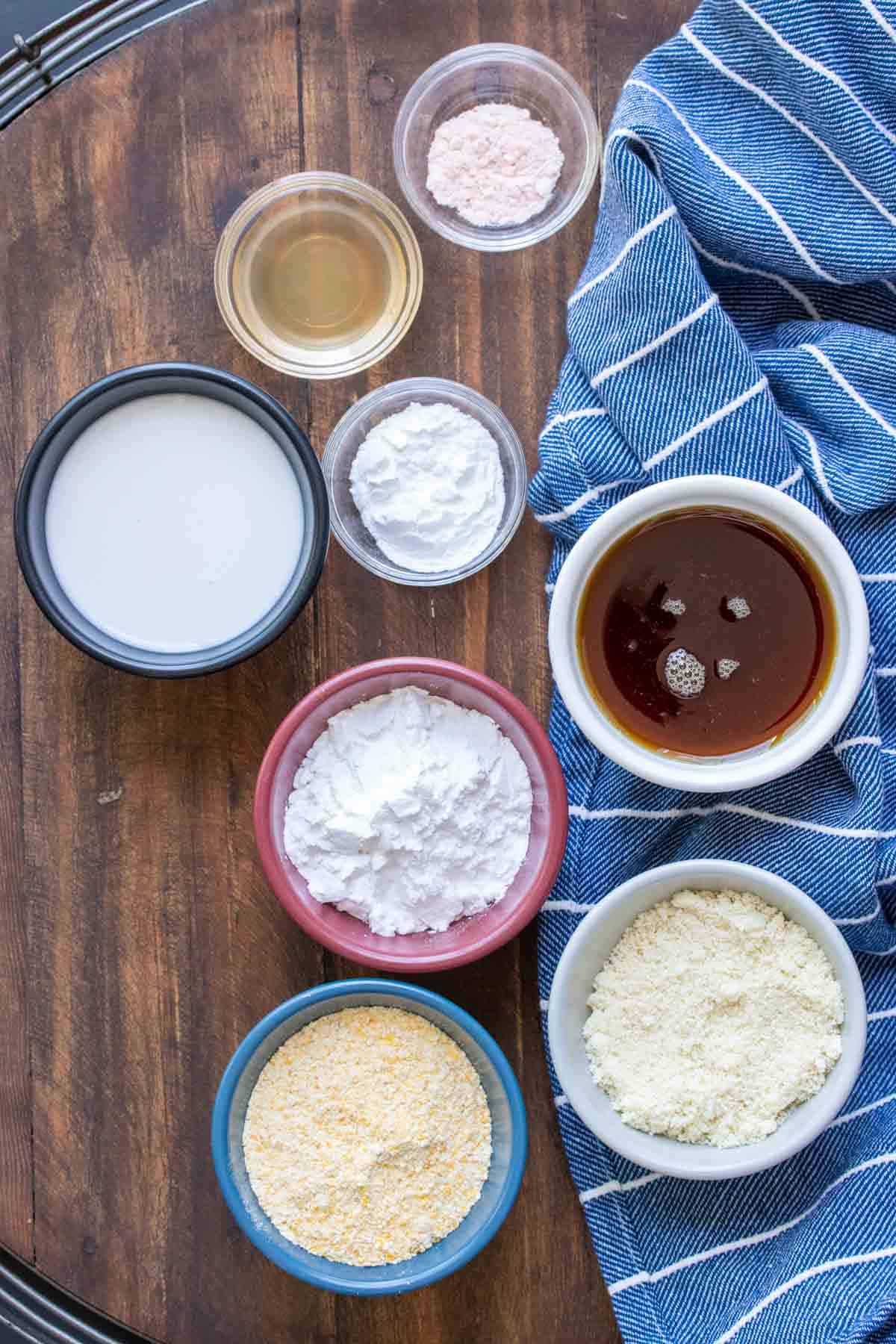 Ingredients needed to make cornbread muffins in different colored bowls next to a blue towel