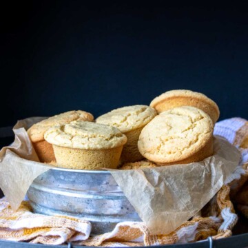 Yellow muffins piled in a metal bowl with parchment paper in it
