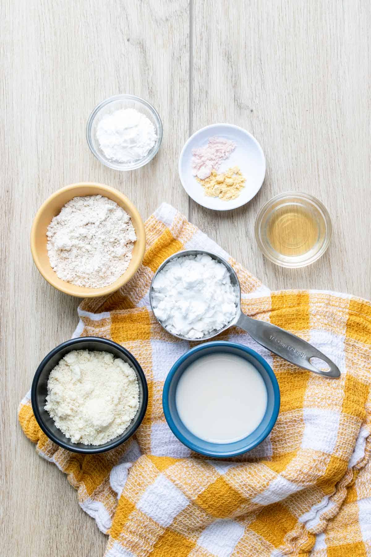 Bowls filled with ingredients needed to make biscuits sitting on a yellow checkered towel