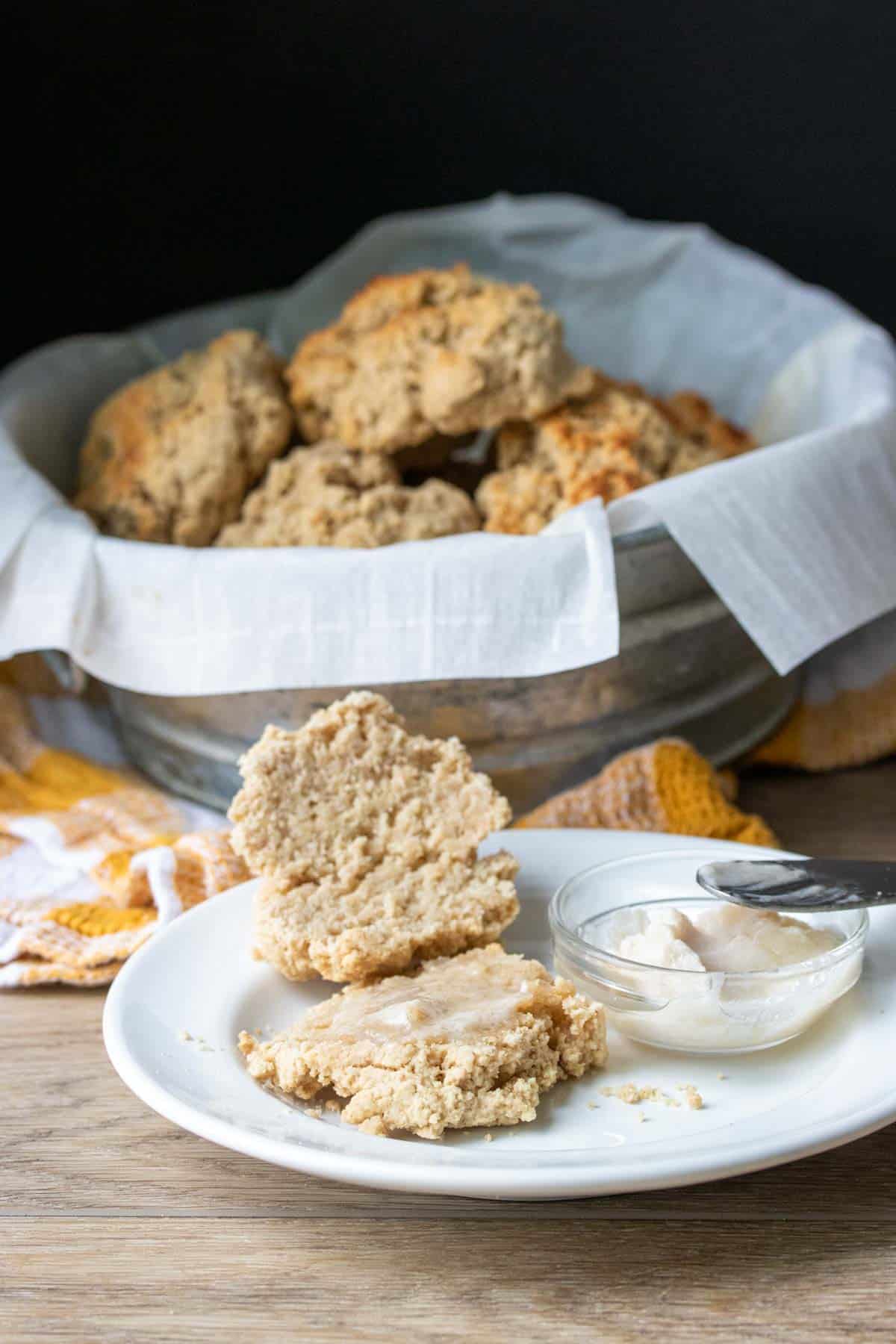 White plate with a biscuit cut in half and topped with batter in front of a tin of them