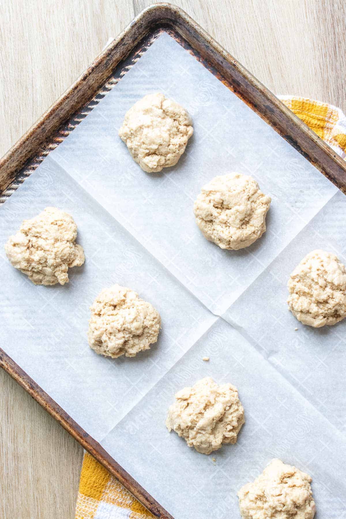 Parchment on a baking sheet topped with raw mounds of biscuit batter