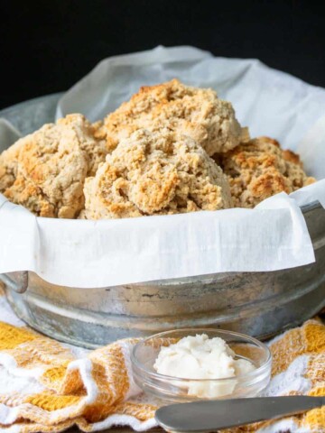 Tin bowl lined with parchment and filled with biscuits sitting on a yellow and white checkered towel