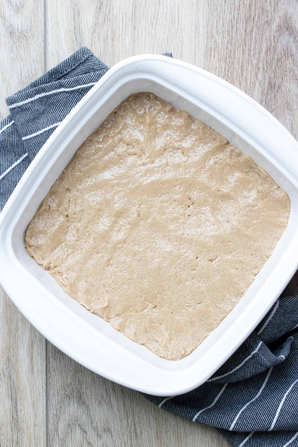 A square white baking dish with shortbread batter pressed into it