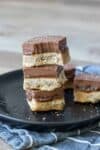 A stack of millionaire shortbread squares on a black plate with the top one half eaten