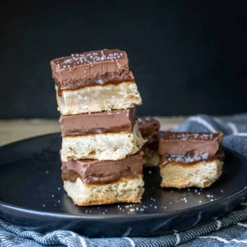 A black plate stacked with squares of millionaire shortbread dessert sprinkled with sea salt