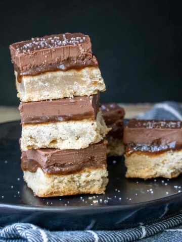 A stack of millionaire shortbread squares on a black plate sitting on a grey blue striped towel