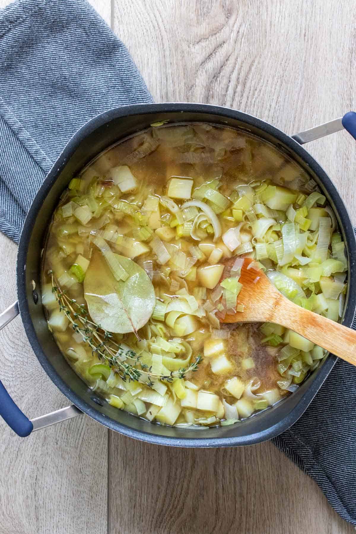 Wooden spoon mixing a broth with potatoes, leeks and herbs in a black pot