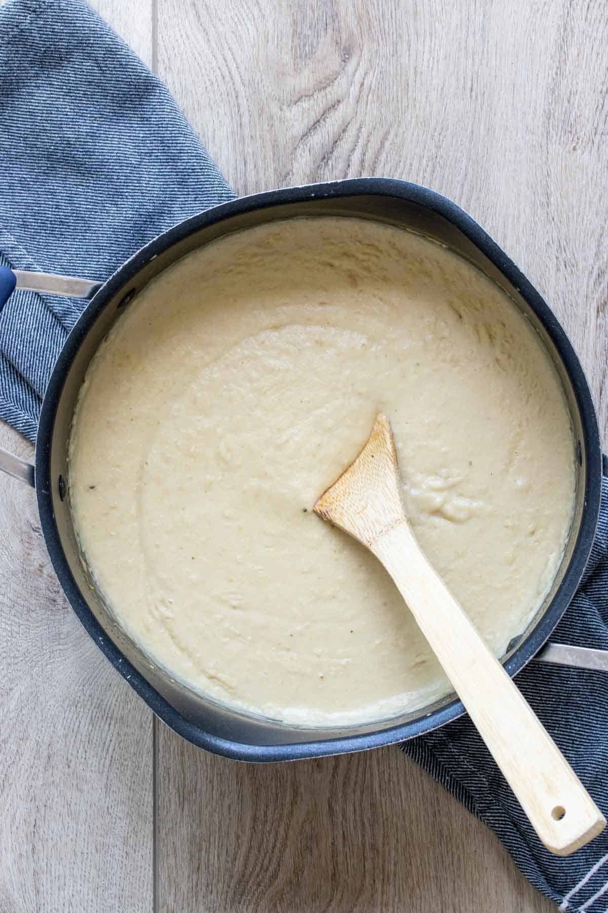 Wooden spoon mixing a thick cream colored soup in a black pot