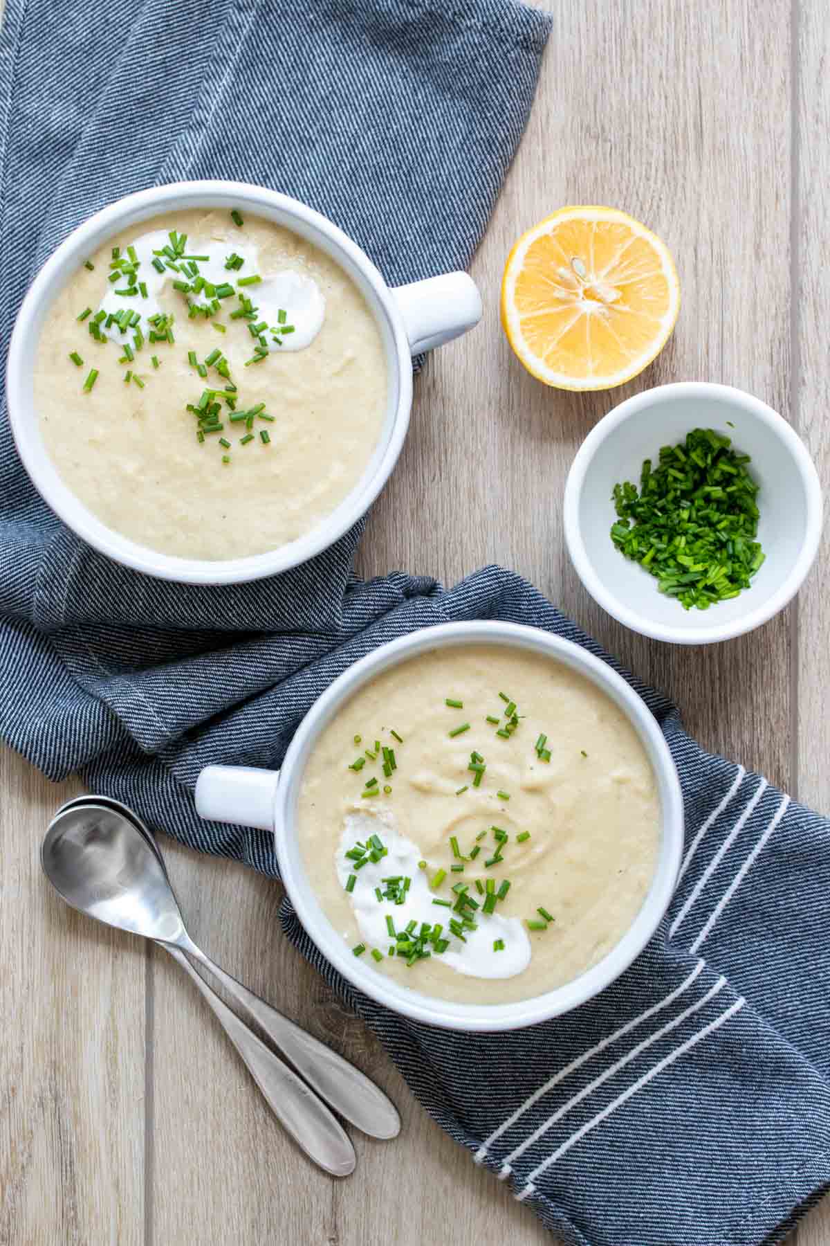 Top view of two white soup bowls on a dark blue towel topped with chopped chives