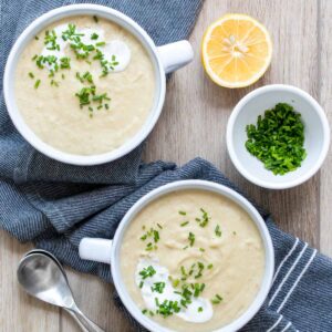 Two white soup bowls with pureed soup next to a cut lemon and white bowl of chives