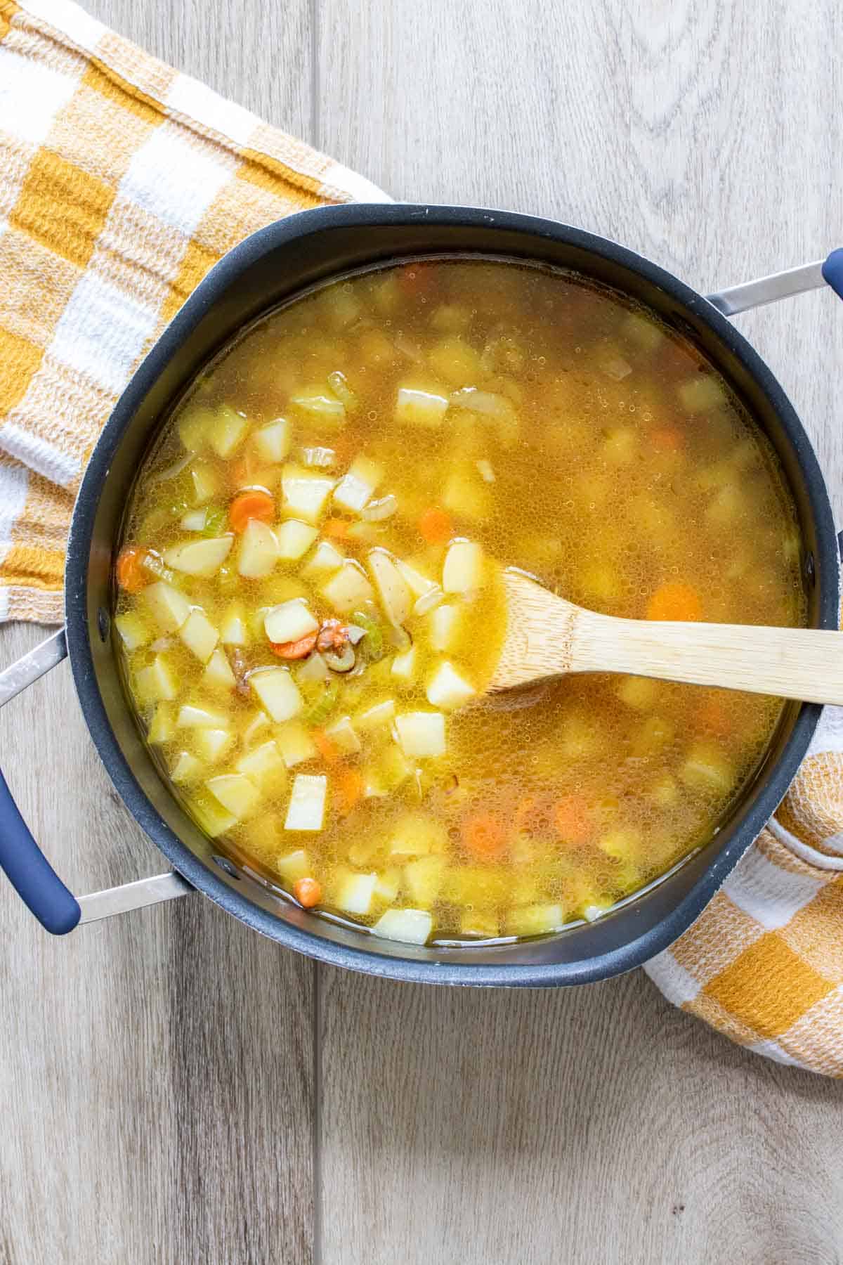 Pot filled with broth, chopped potatoes and carrots with a wooden spoon