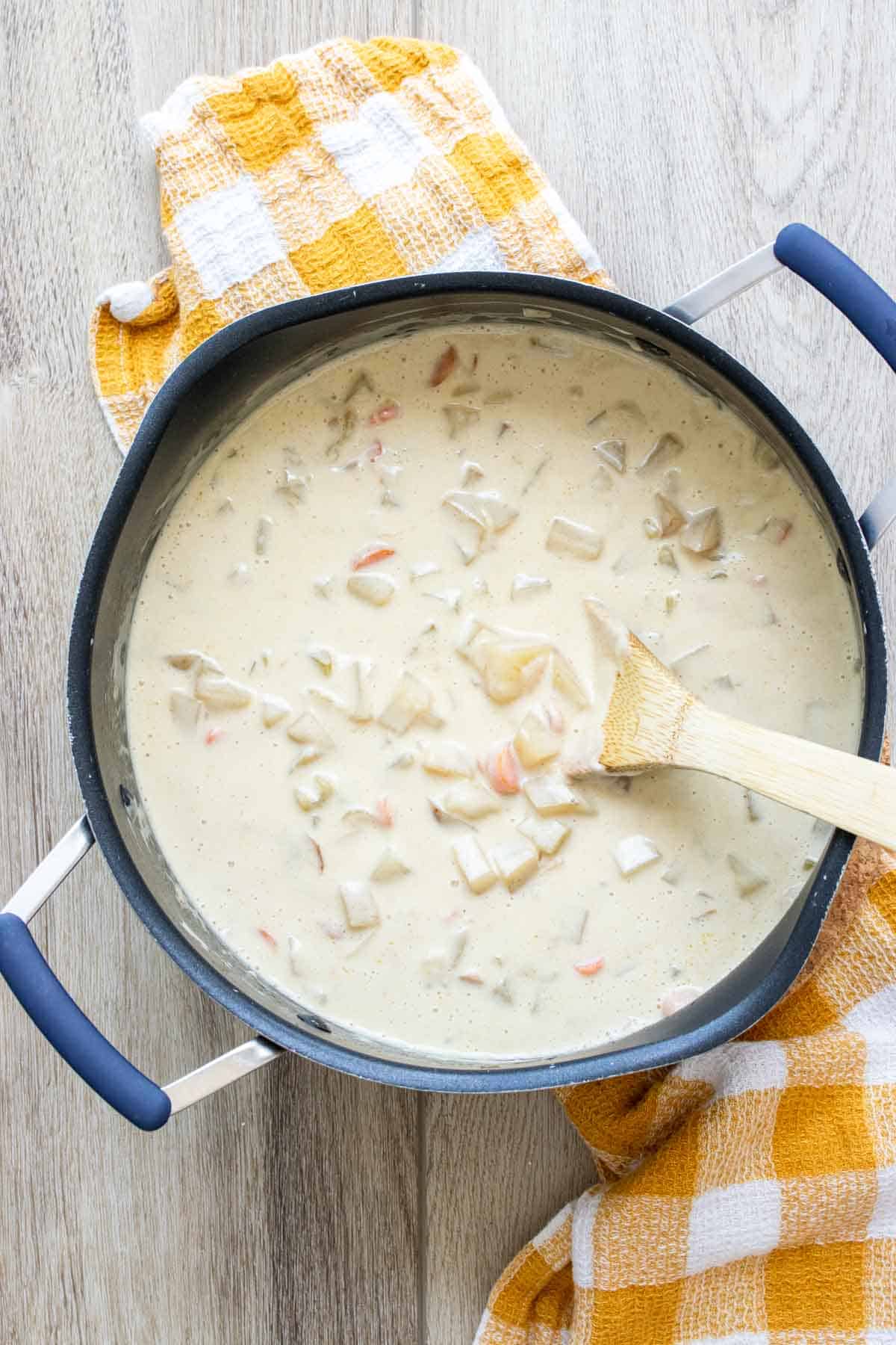 Wooden spoon mixing a creamy vegetable soup in a black pot