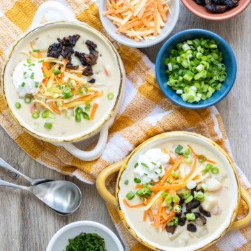 Two bowls of fully loaded potato soup on a yellow and white checkered towel next to toppings