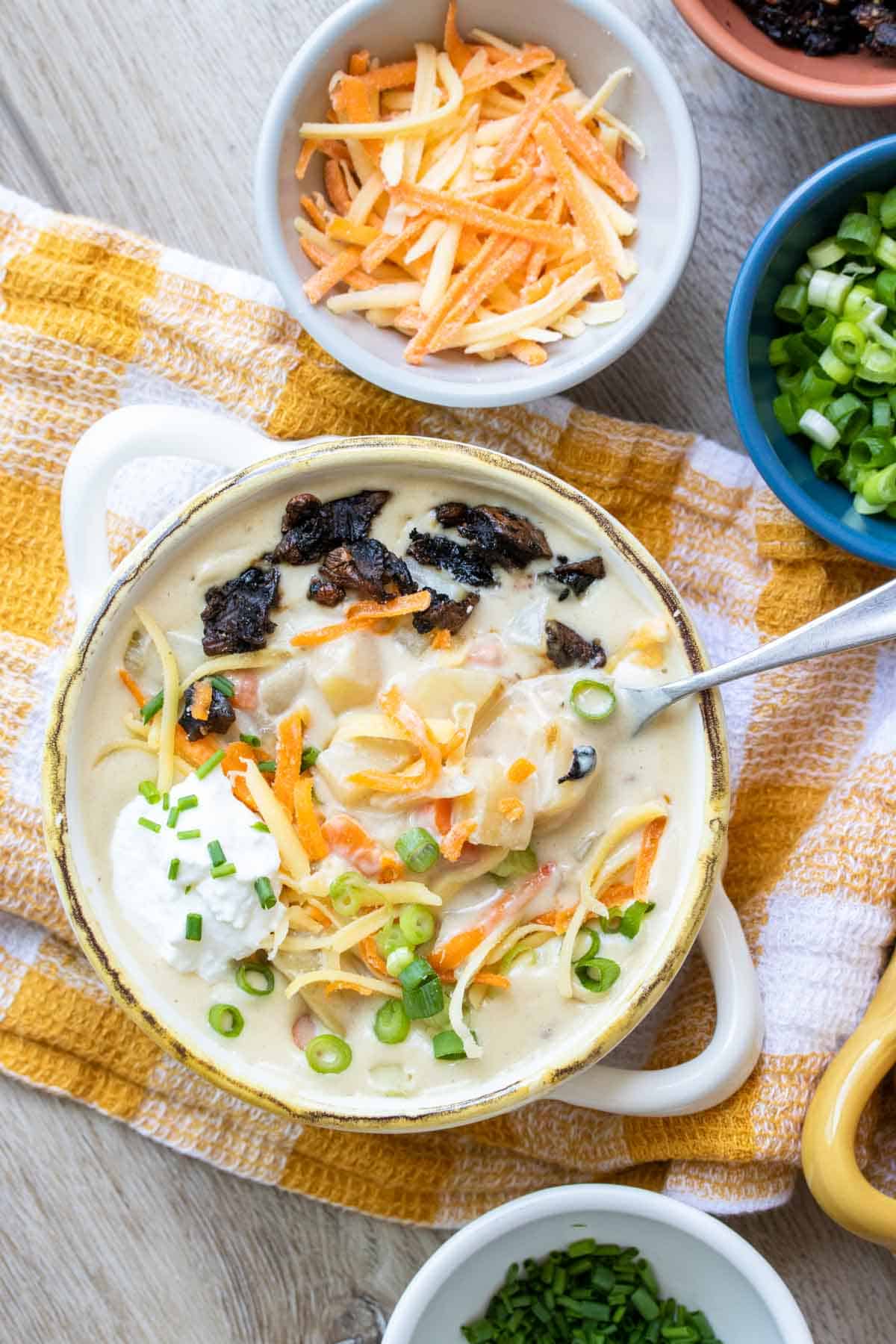 Spoon getting a bite from a cream bowl with potato soup covered in toppings
