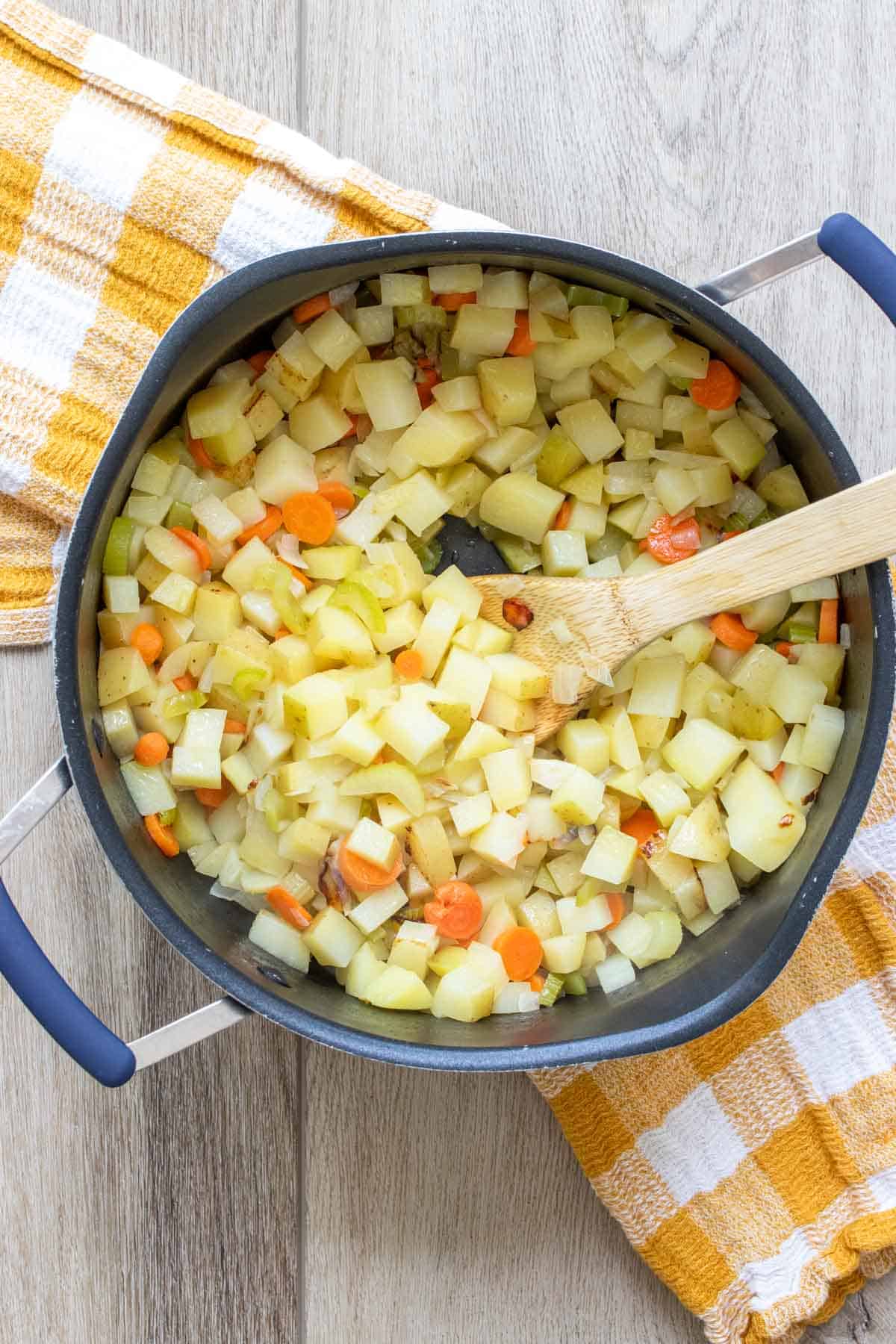 Wooden spoon mixing chopped potatoes and carrots in a black pot