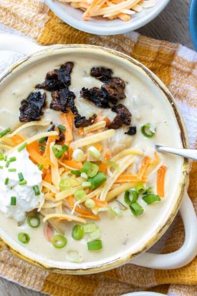 Cream bowl with creamy soup inside topped with sour cream, cheese, scallions and bacon