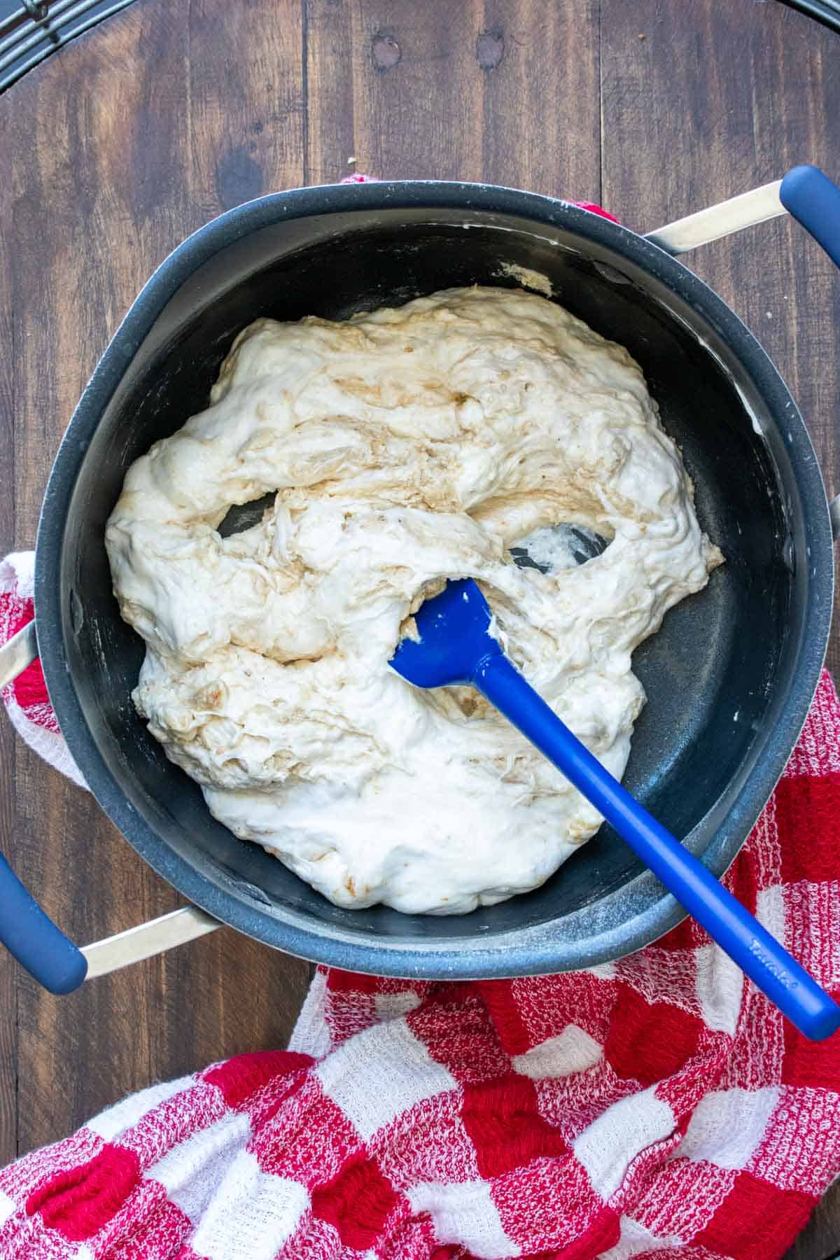 Blue spatula mixing melted marshmallows in a black pot