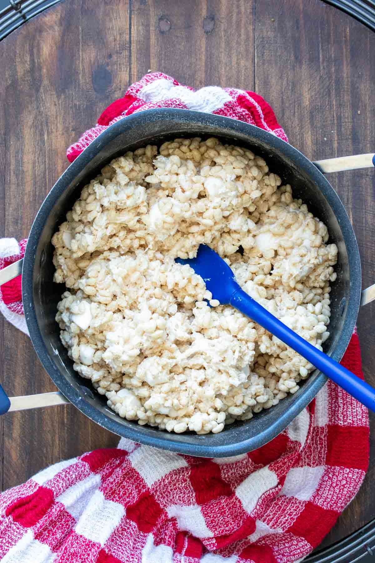 Spatula mixing rice cereal and marshmallows in a black pot