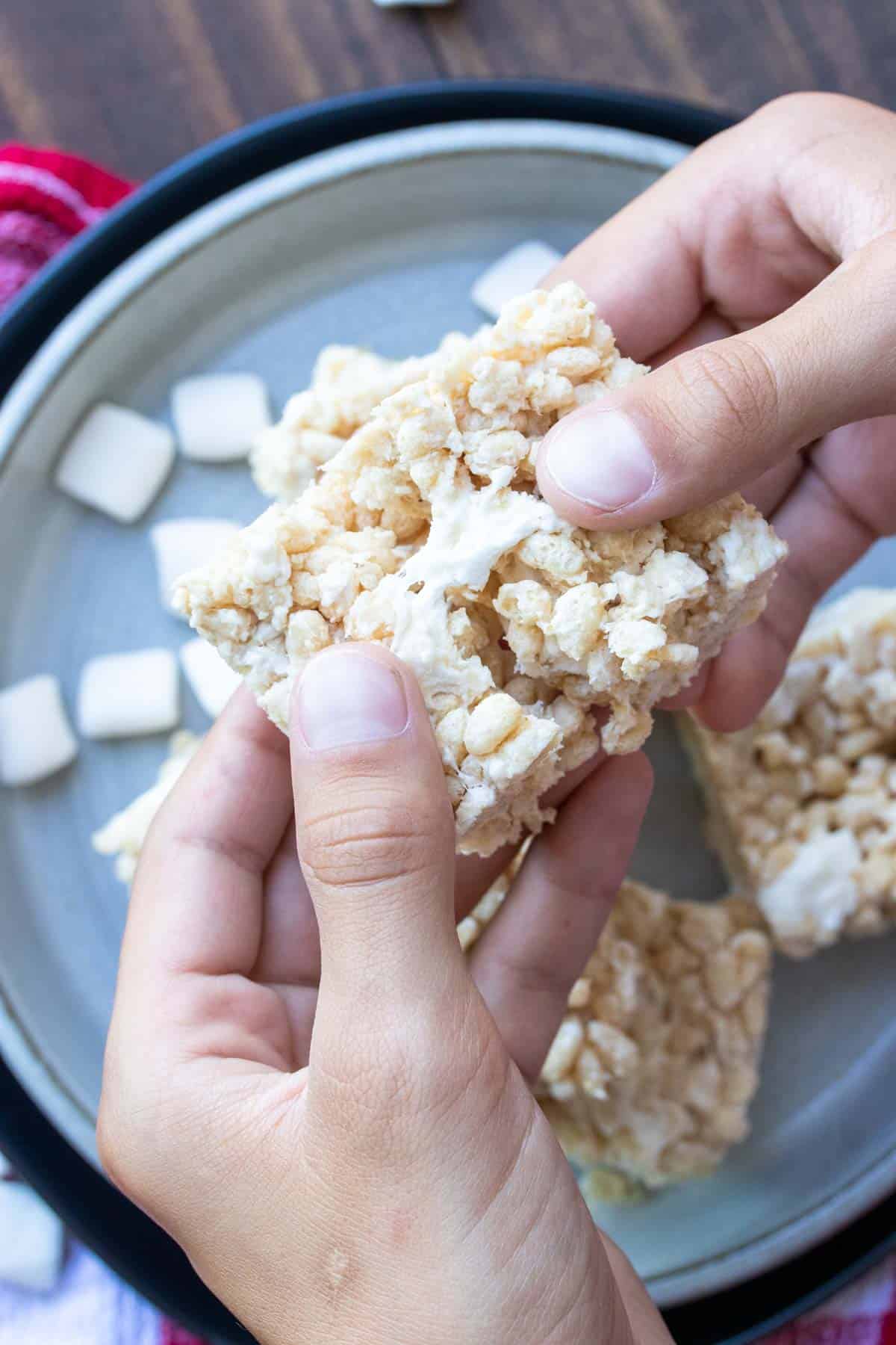 Hand pulling apart a rice krispie treat over a grey plate