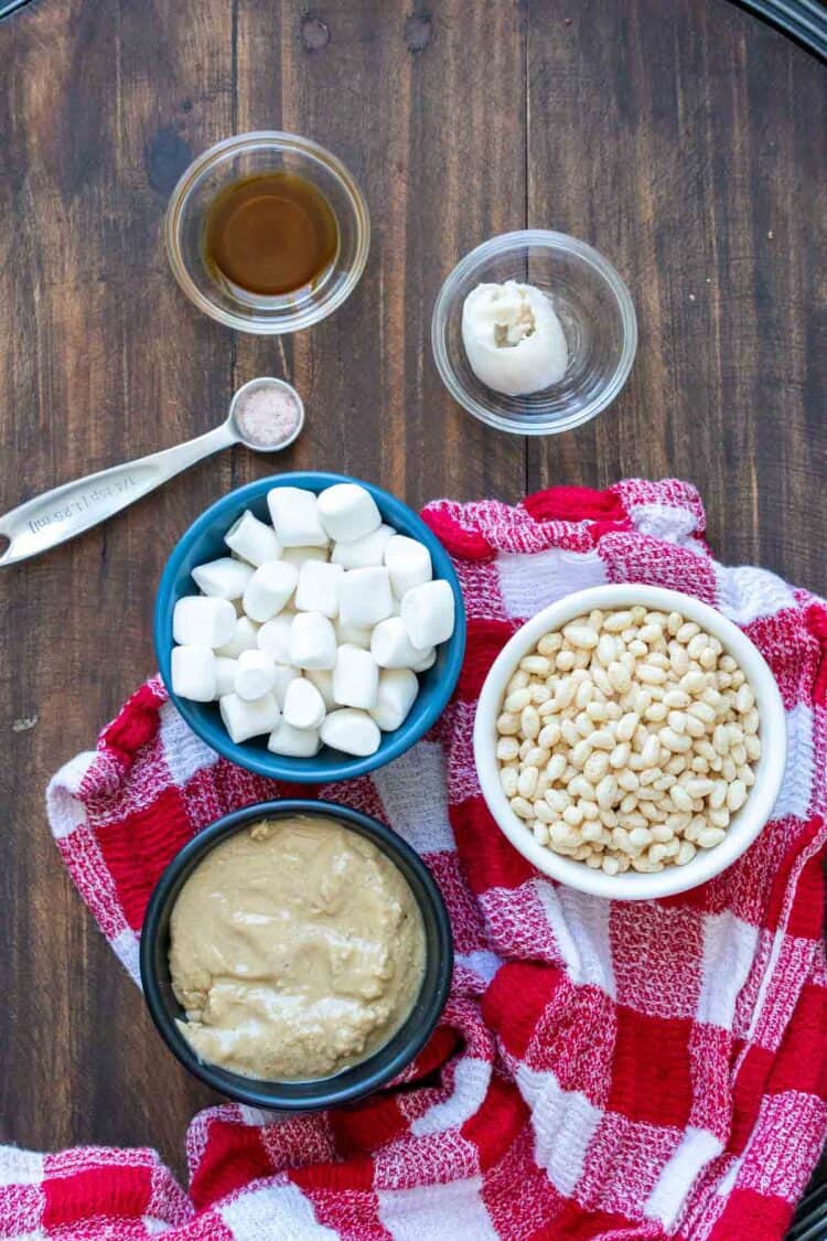 Bowls with ingredients to make rice krispie treats on a wooden surface with a checkered towel