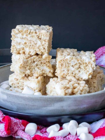 A grey plate sitting on a red checkered towel piled high with rice krispie squares