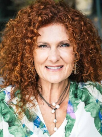 Woman with red curly hair and a green palm leaf shirt smiling