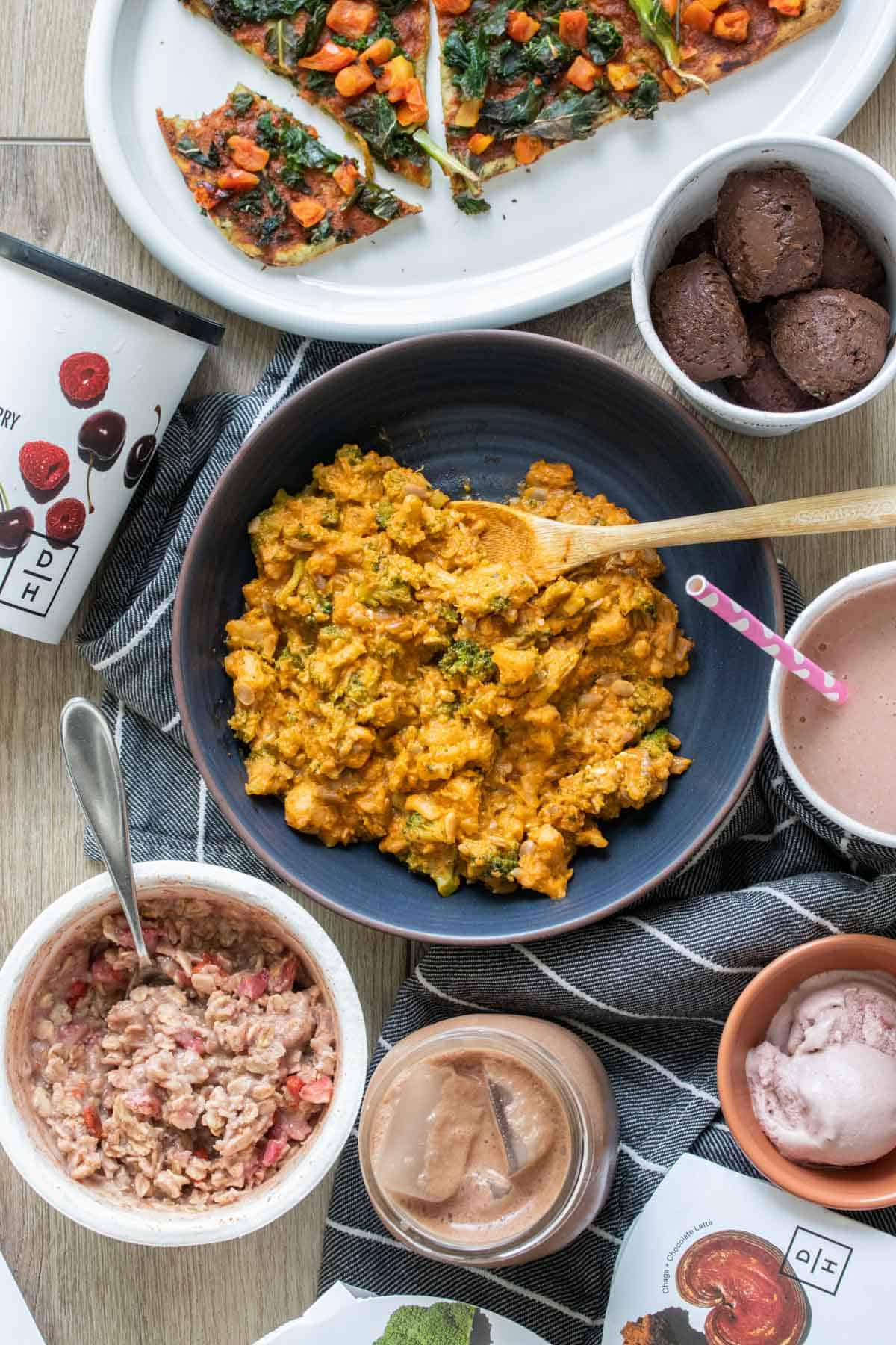 Top view of a blue bowl filled with an orange colored rice dish surrounded by food like pizza, ice cream, oats and drinks