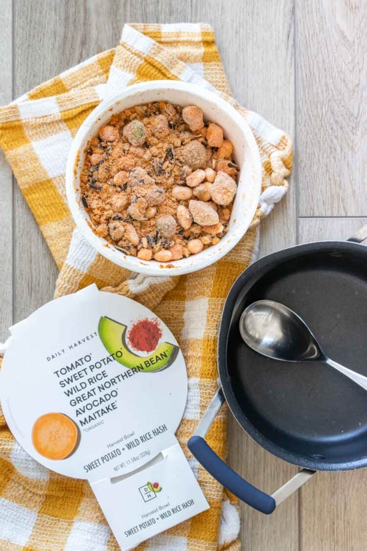 Top view of a frozen meal in a white paper bowl with the packaging next to it and a black pot